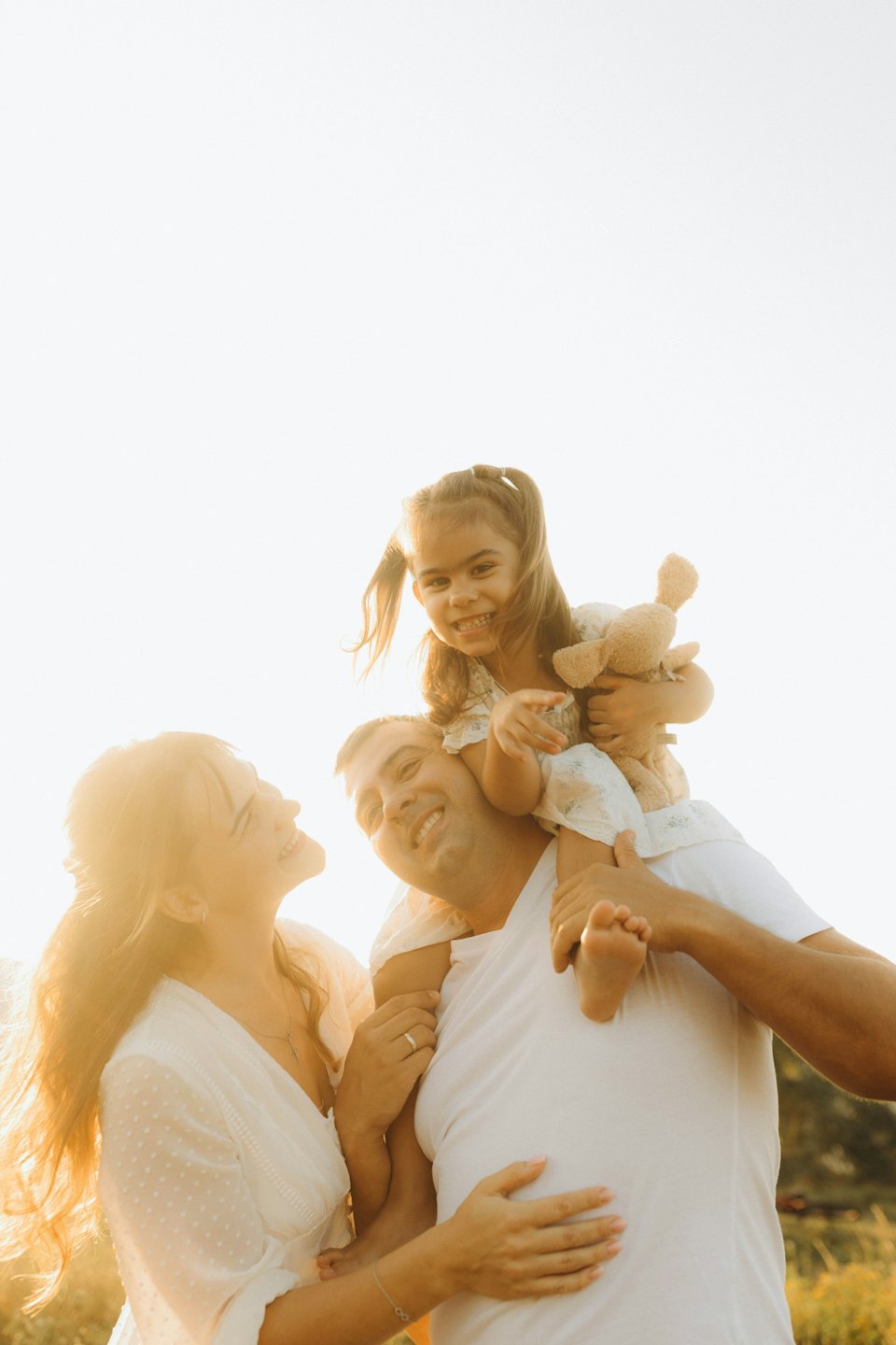 A father carries his daughter on his shoulders beside her mother.
