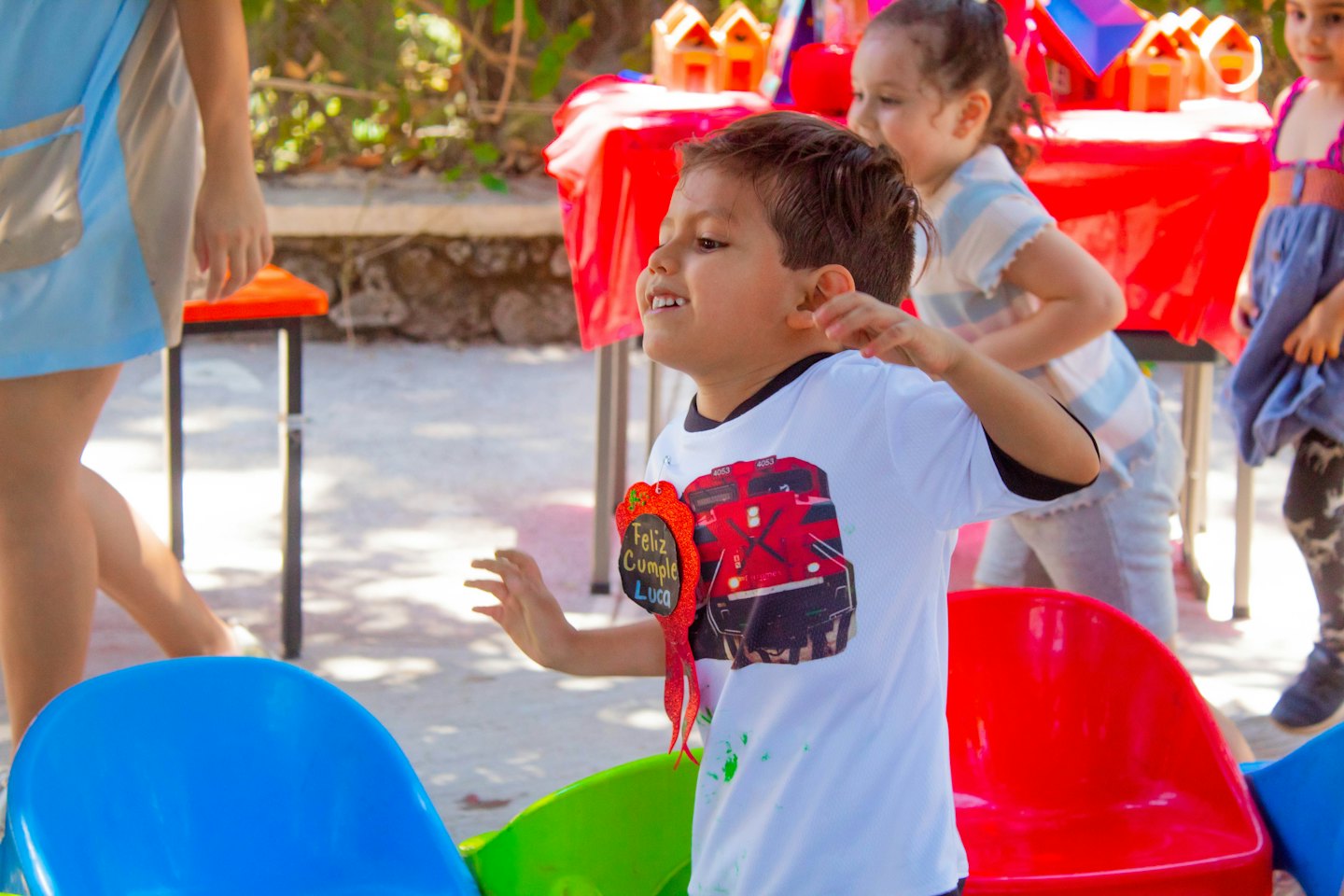A boy wearing a birthday badge smiles at an outdoor party.