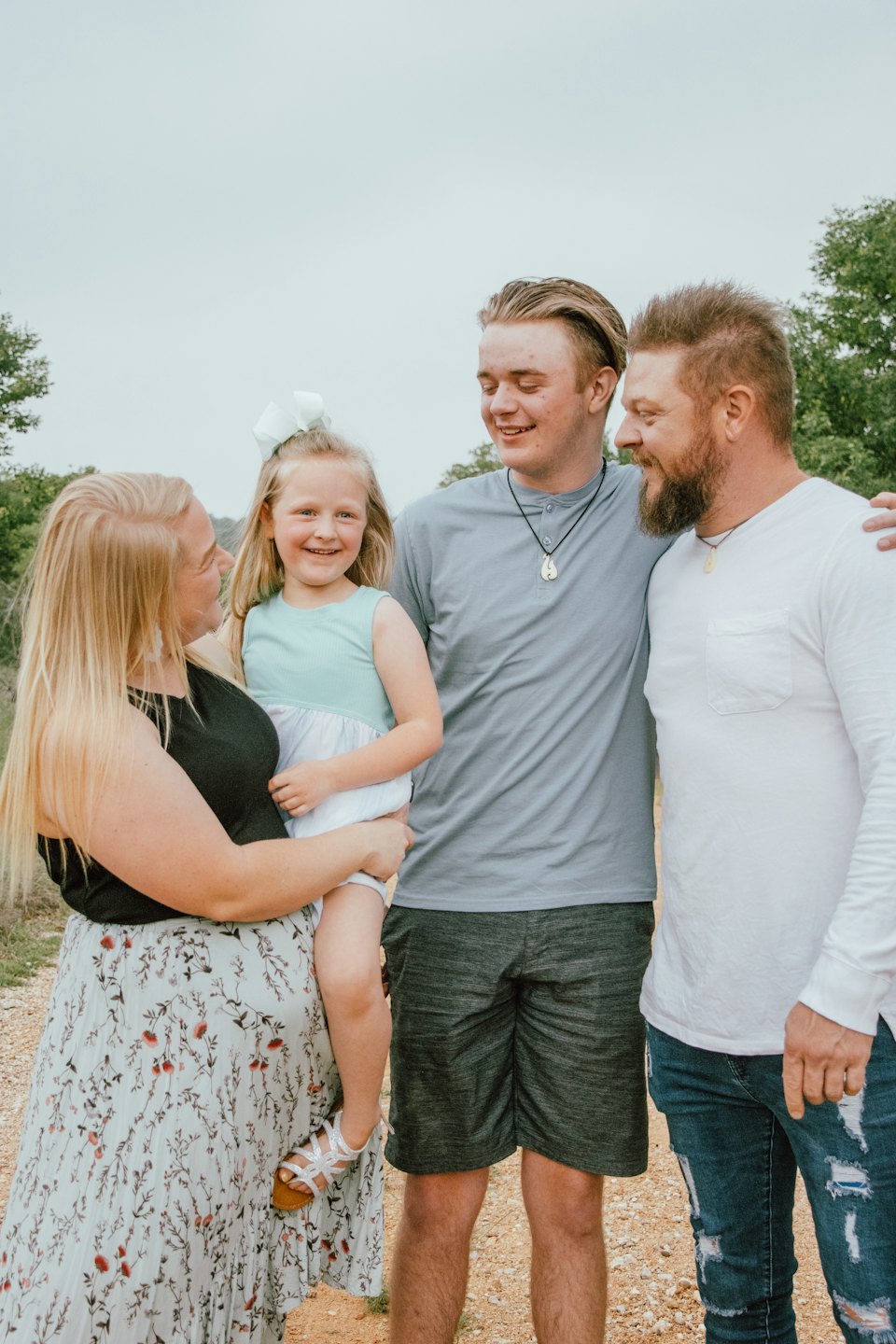 Family standing and smiling together on a dirt path.