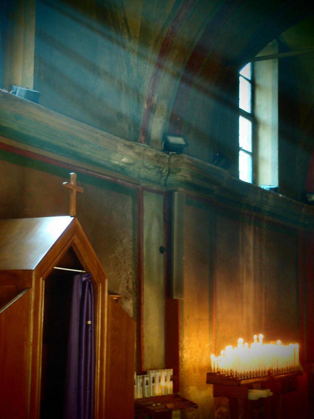 Sunlight streams through a church window onto the ceiling and confessional.